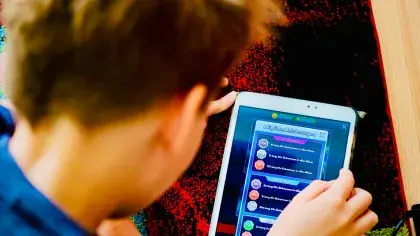 Junge von hinten schaut auf sein Tablet, wo er ein Spiel spielt